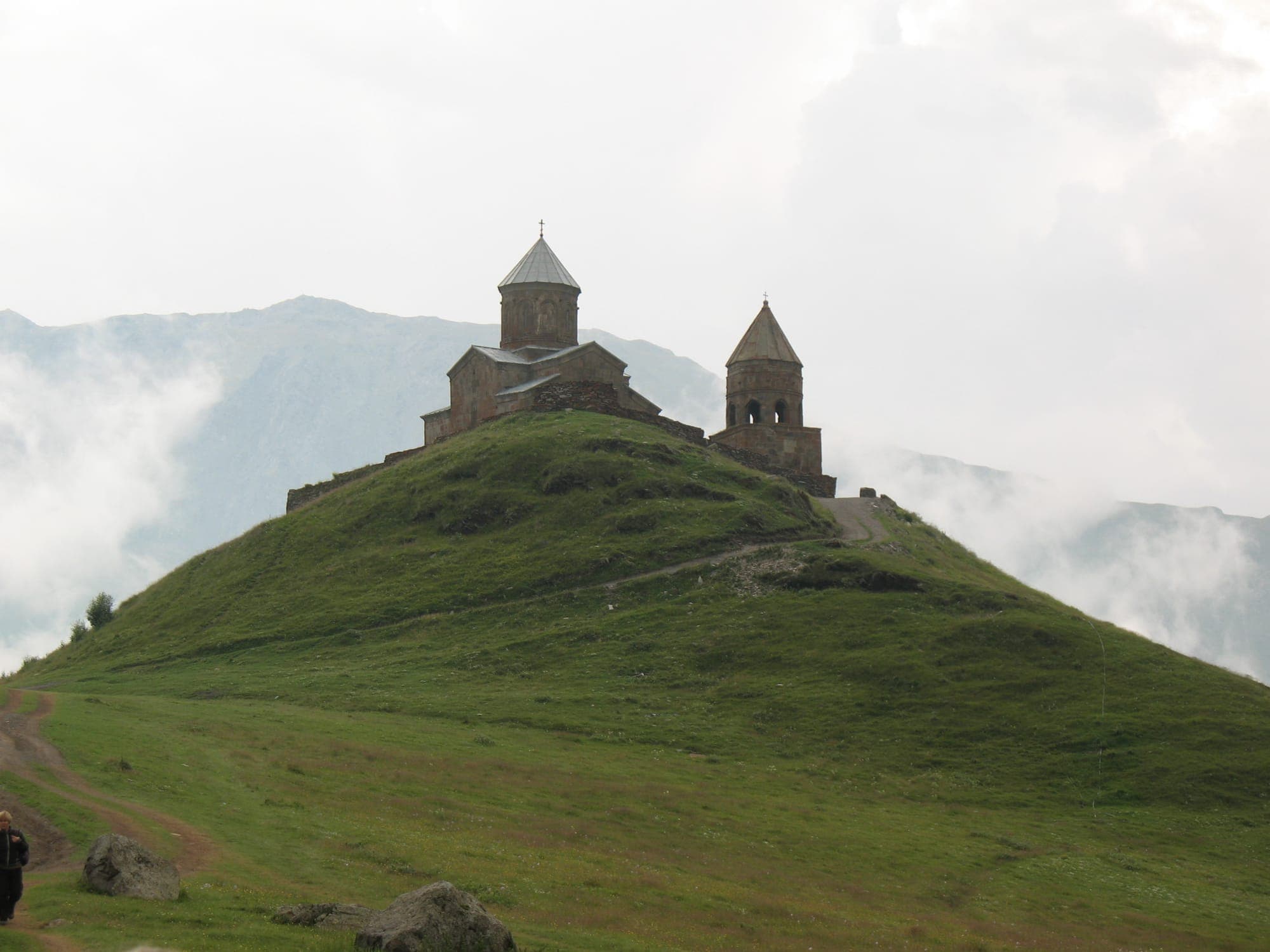 Gergeti Trinity Church on a green hilltop below the snowy Caucasus mountains
