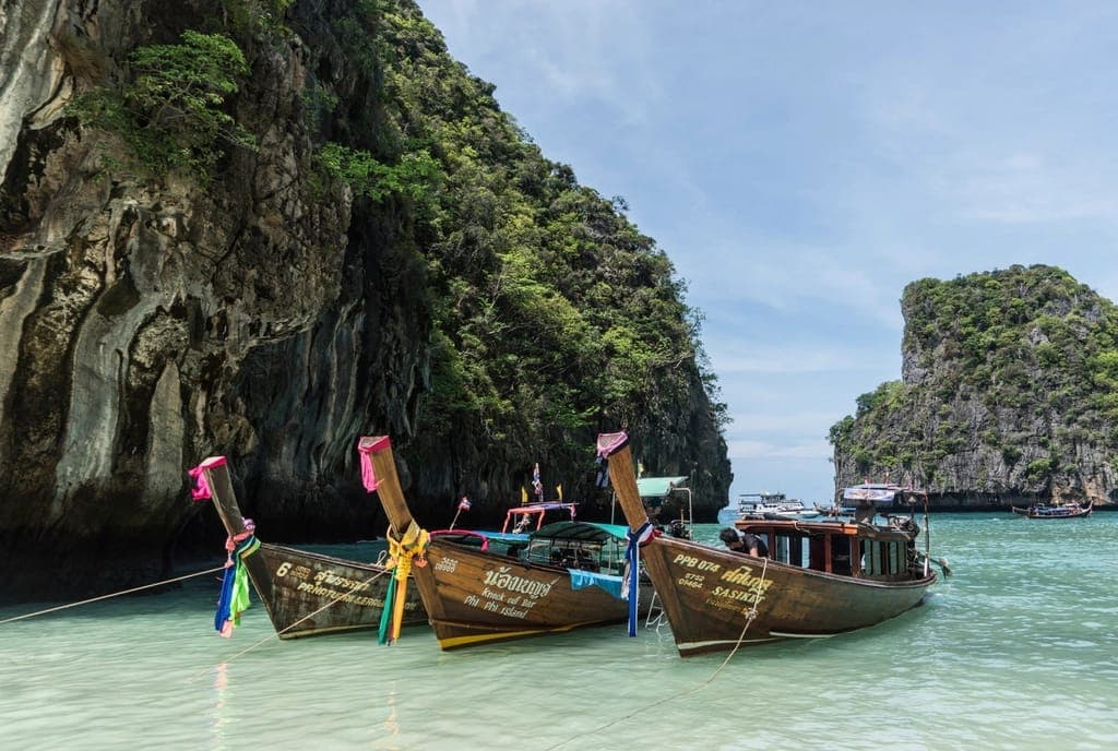 Longtail boats moored on a turquoise bay below limestone cliffs in southern Thailand